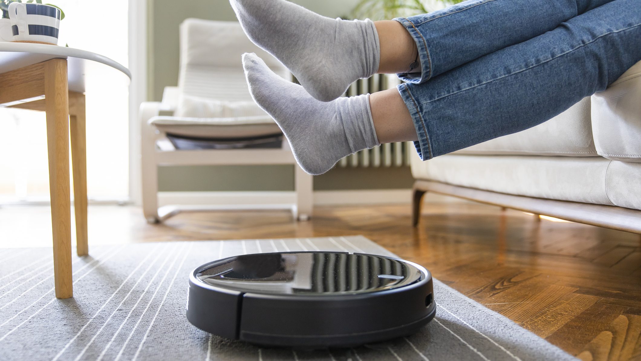 Young woman lift up the feet for letting robotic vacuum cleaner pass though