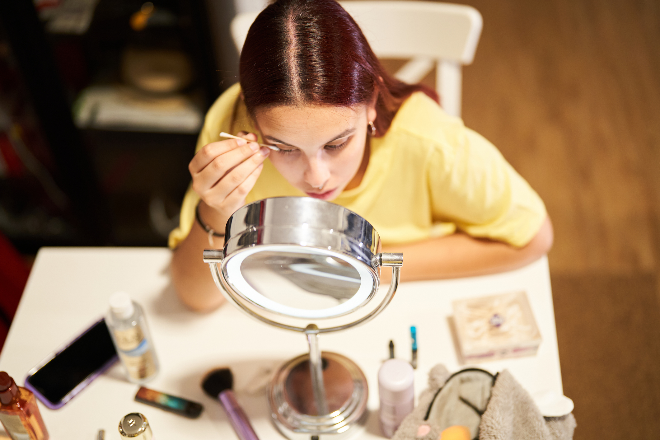 A girl doing her eyelashes in front of a makeup mirror.