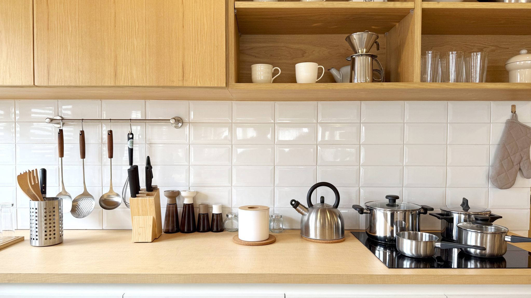 Clean and organized modern kitchen interior with wooden cabinets, white tiled backsplash, and stainless steel appliances. Minimalist Scandinavian style, cozy home cooking space. Bright and inviting.