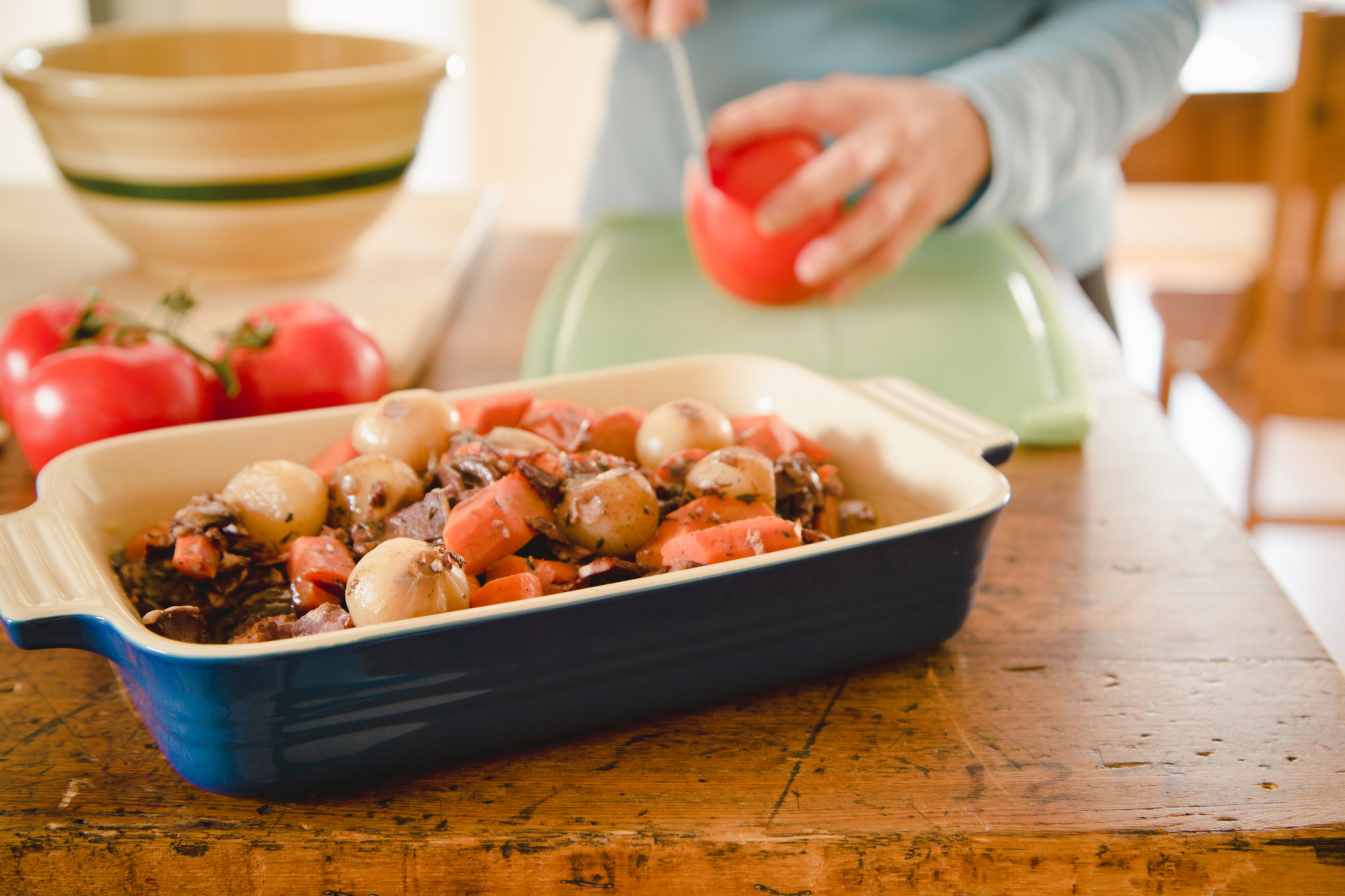 A woman making beef stew in a casserole dish.