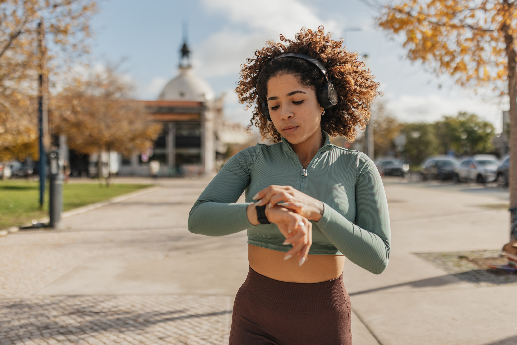 A focused woman checks her fitness tracker while jogging outdoors, symbolizing dedication to health and the integration of technology in personal fitness endeavors.