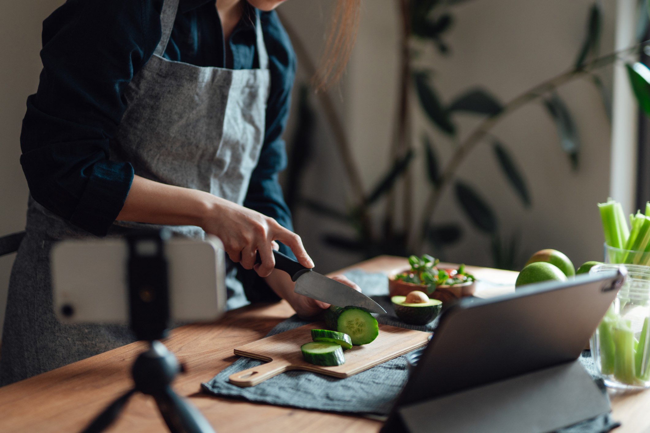 Cropped shot of young woman making vegan meals while vlogging with smartphone and digital tablet. Online remote learning. Healthy eating and vegan lifestyle.