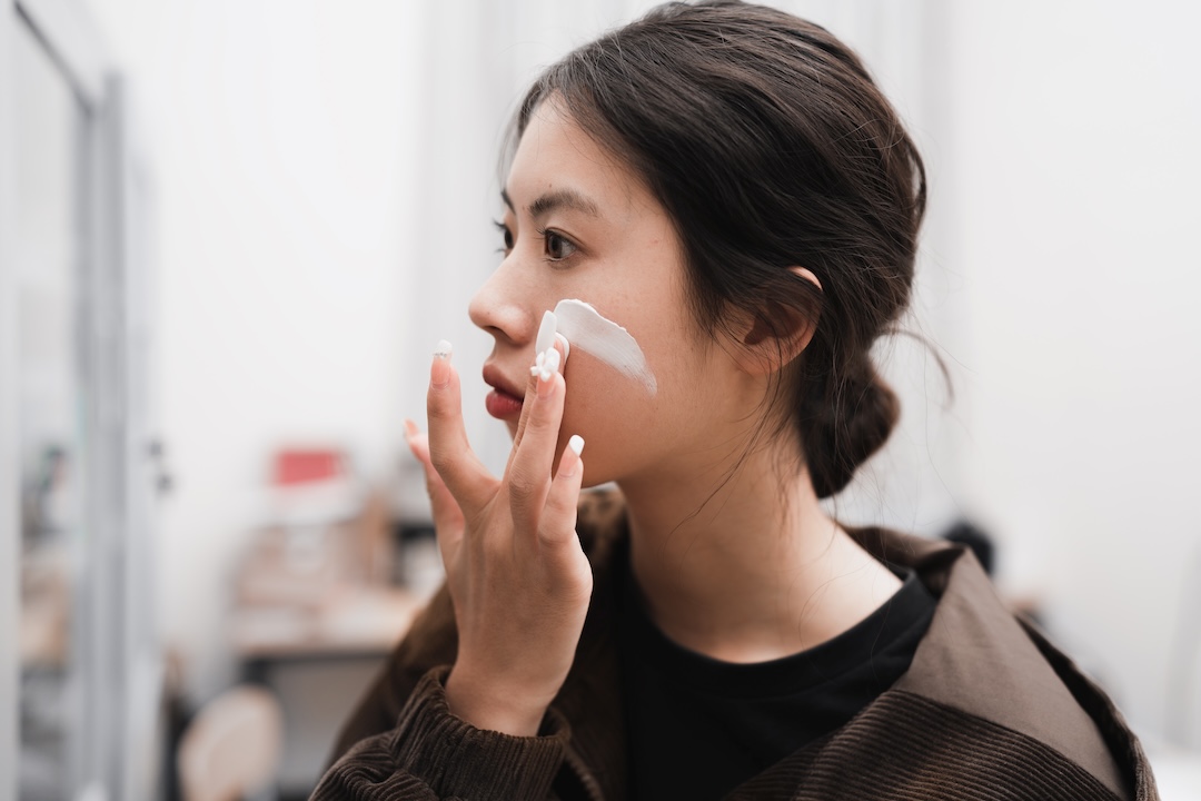 Woman looks into the mirror and applies makeup to her face with her hands