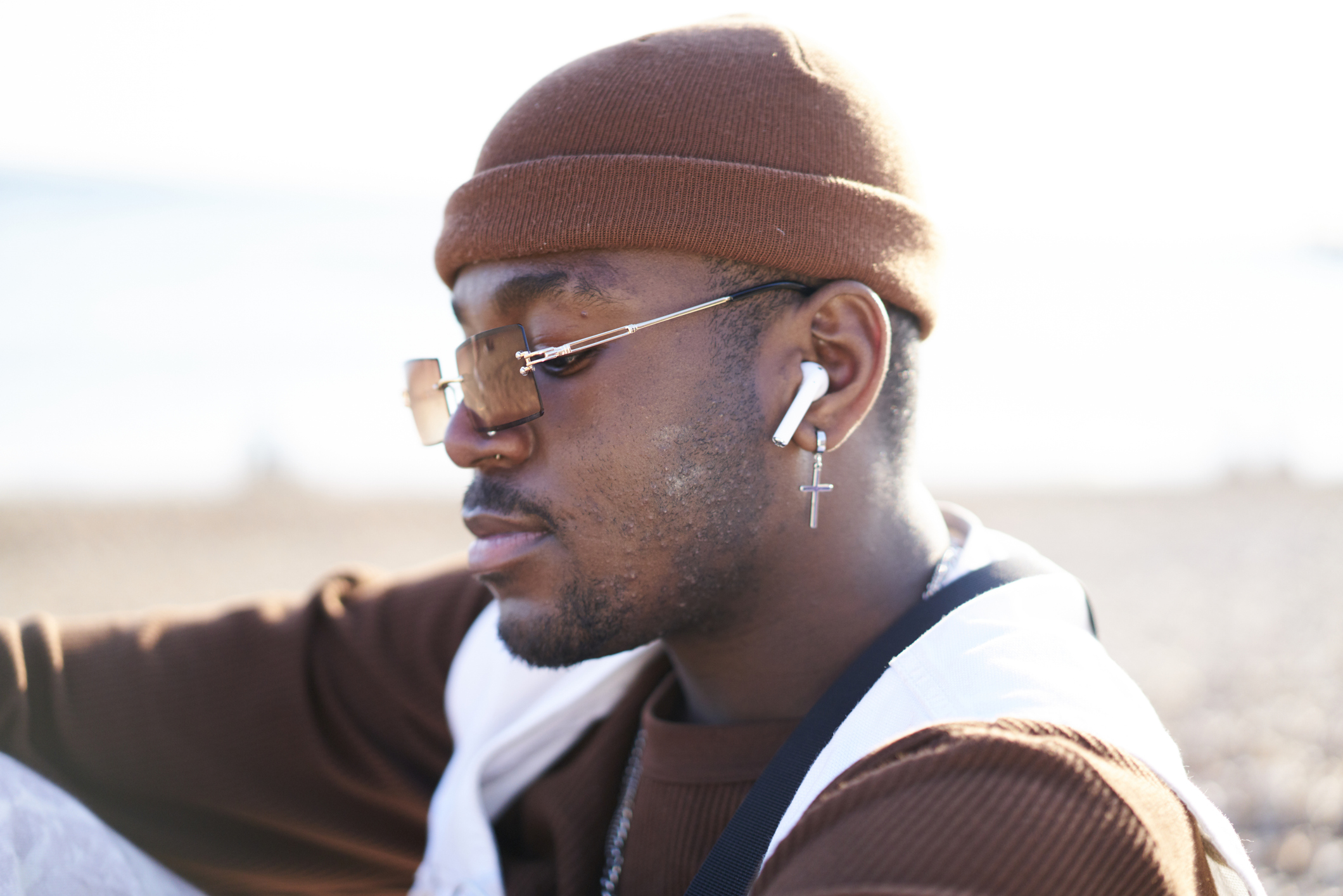 Fashionable young man sitting enjoying a moment on the beach listening to music on wireless earbuds