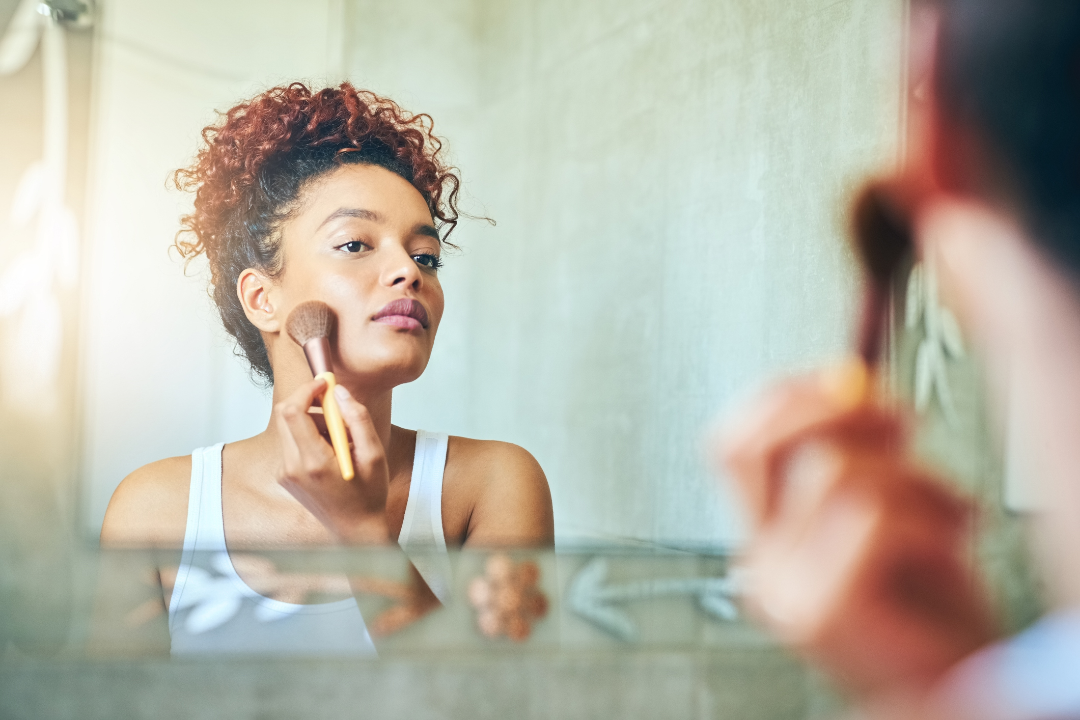 Shot of a young woman using a makeup brush while looking in her bathroom mirror