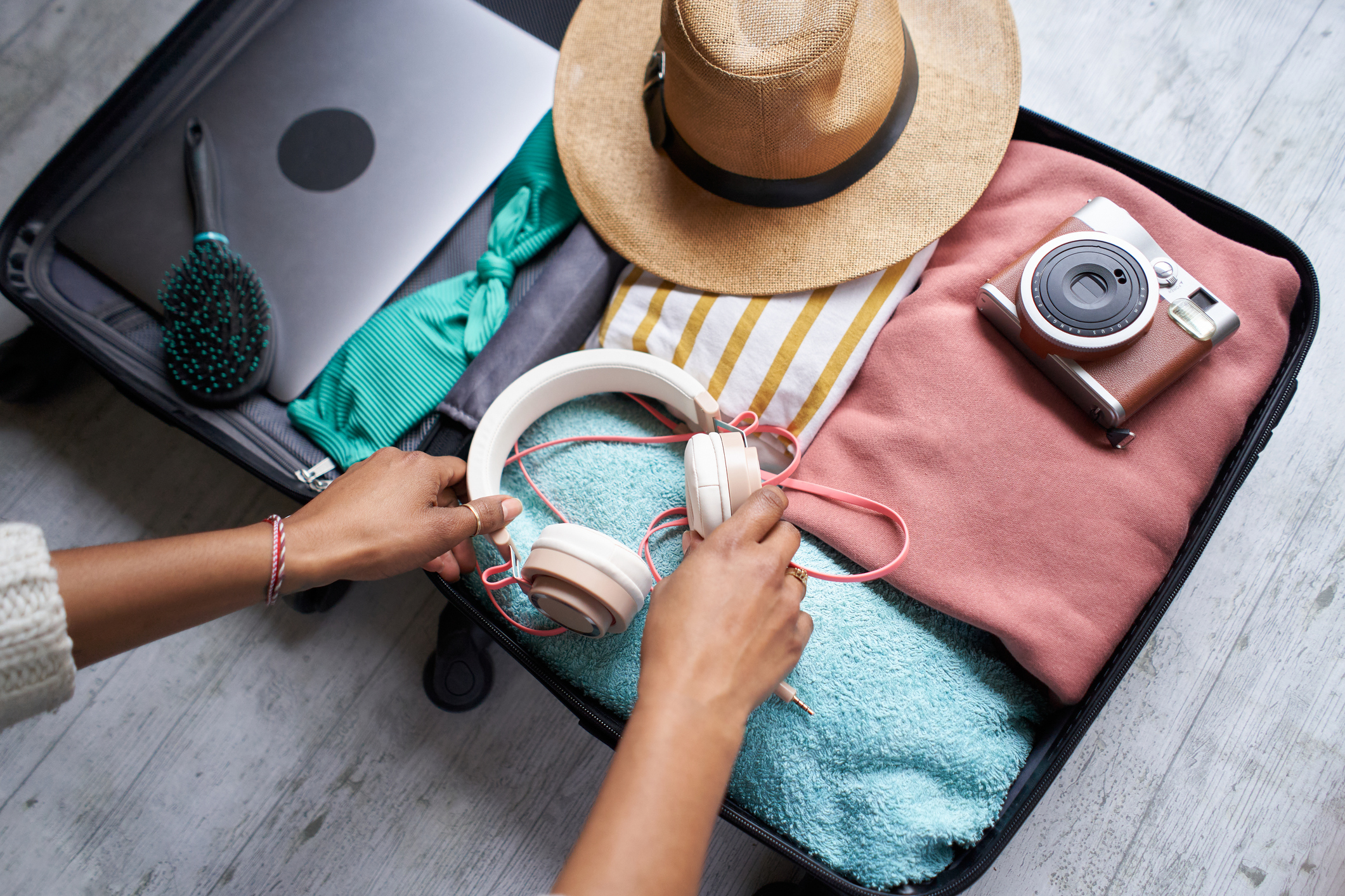 Photo of an open luggage filled with summer items ready to go on holidays, woman's black arms organizing it.