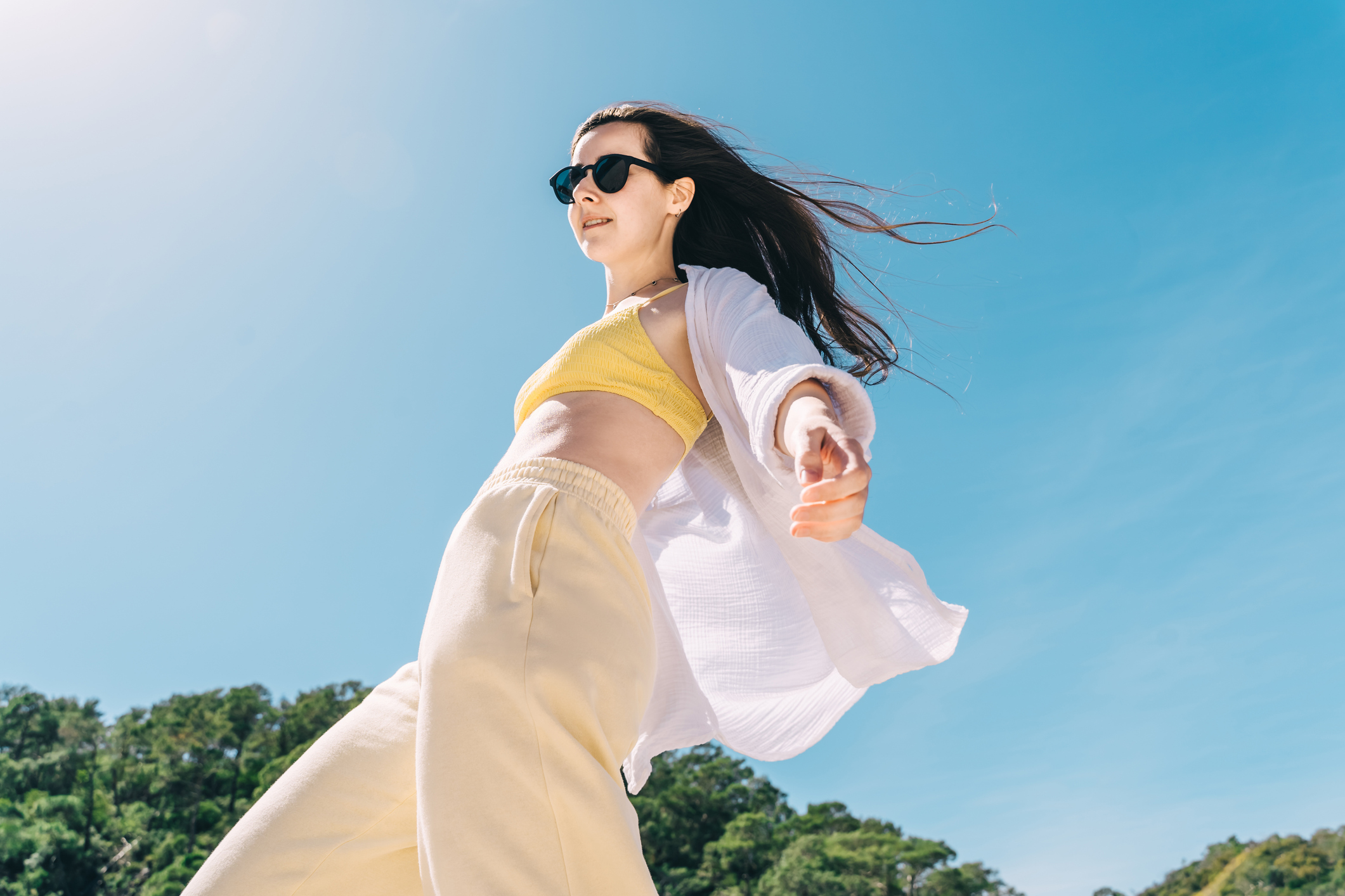 Beautiful young woman in sunglasses and white muslin shirt have a fun on the beach, blue sky on background. Bottom view.