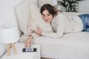 Young woman lying on bed switching off smart phone alarm at home
