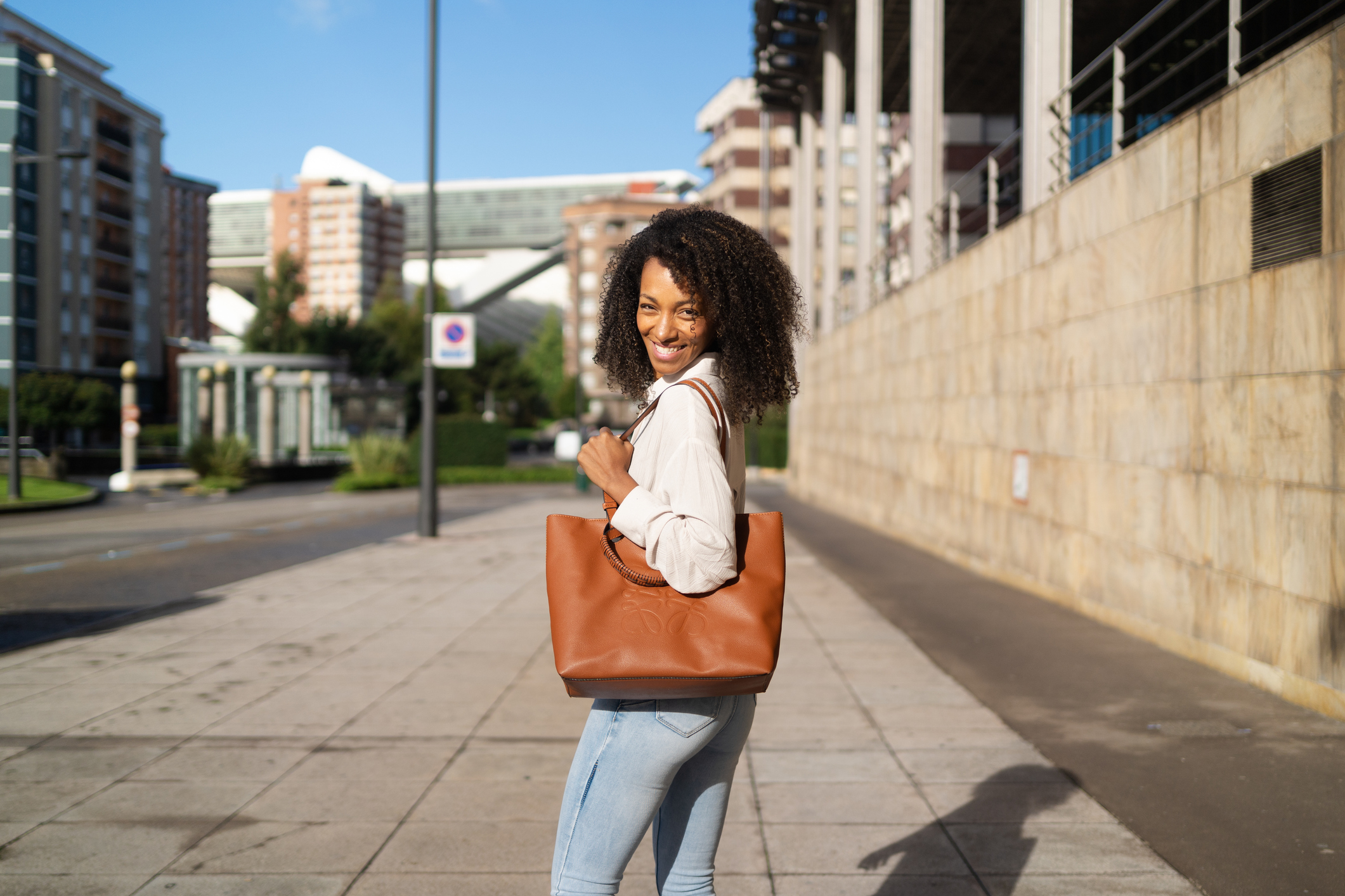 Stylish young woman is holding her brown leather purse while walking down a city sidewalk