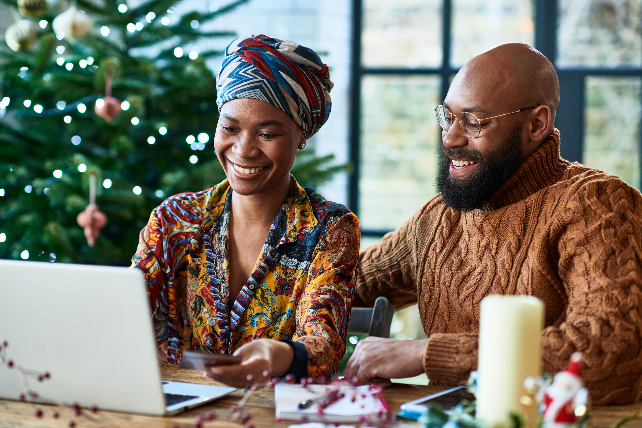 Mid adult man and woman sitting at table covered with Christmas decorations, using the internet, online, video call