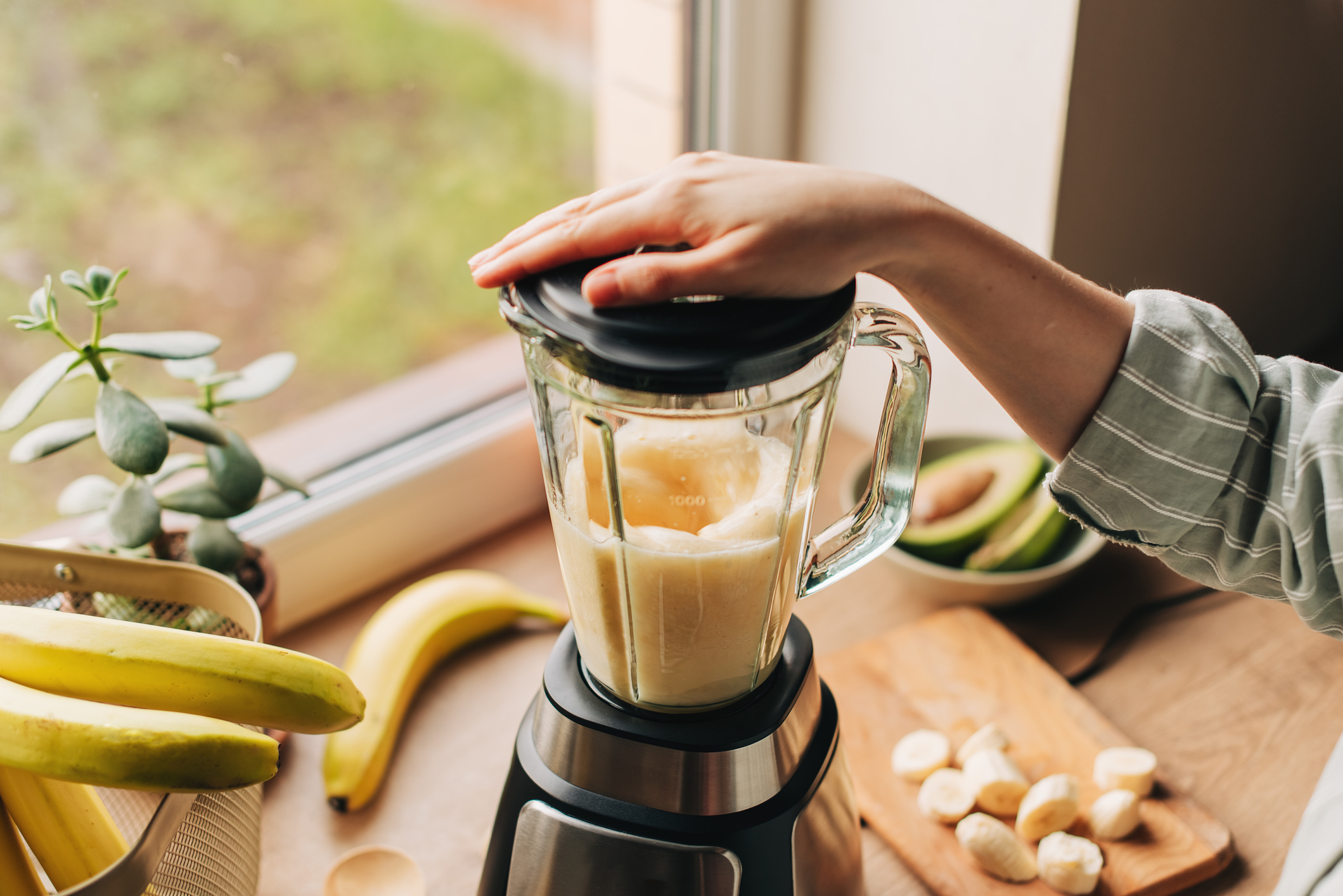 Woman blending spinach, berries, bananas and almond milk to make a healthy green smoothie