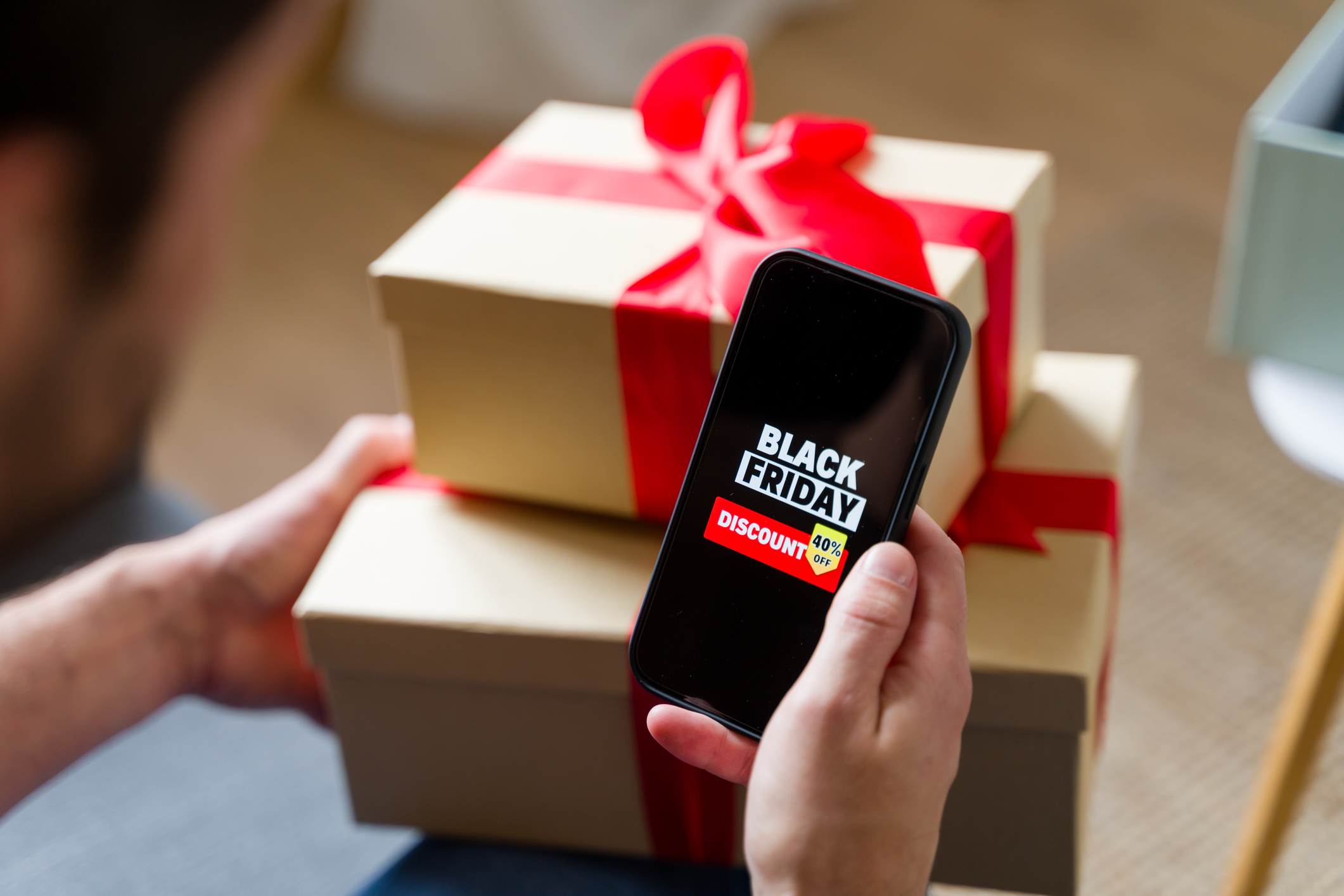 Man is holding a smartphone with black friday discount on screen and gifts in the background