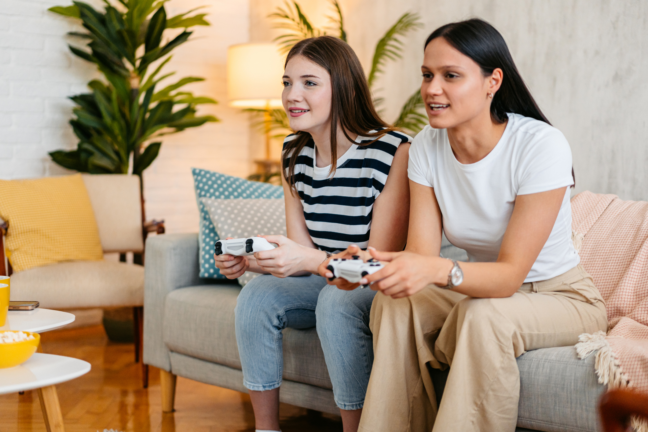 Two female friends playing video game on a joystick in the living room.