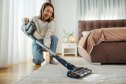 Young asian woman vacuuming carpet in her bedroom, smiling, performing daily household chores with a modern appliance