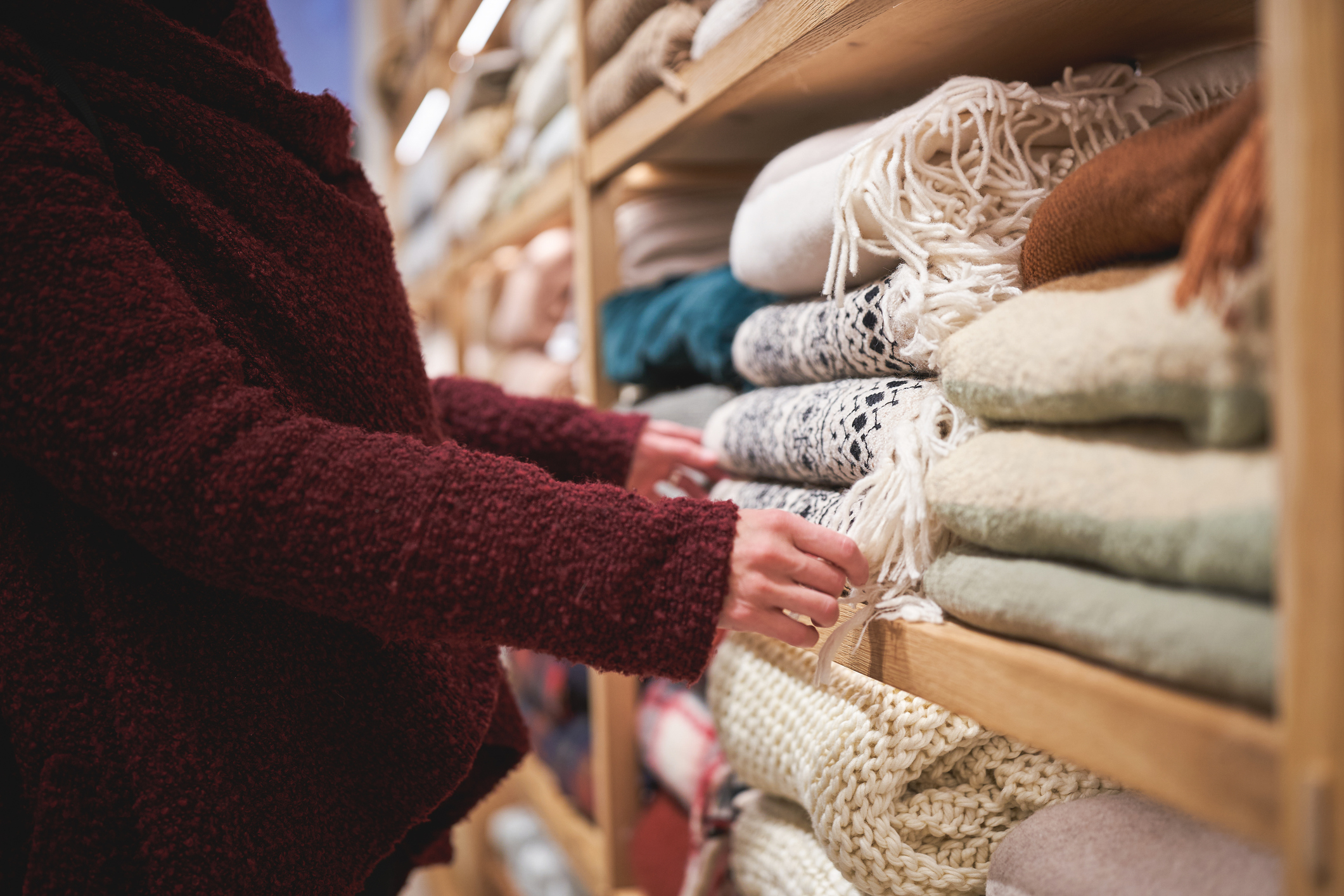 Hands touching soft folded blankets in cozy store interior