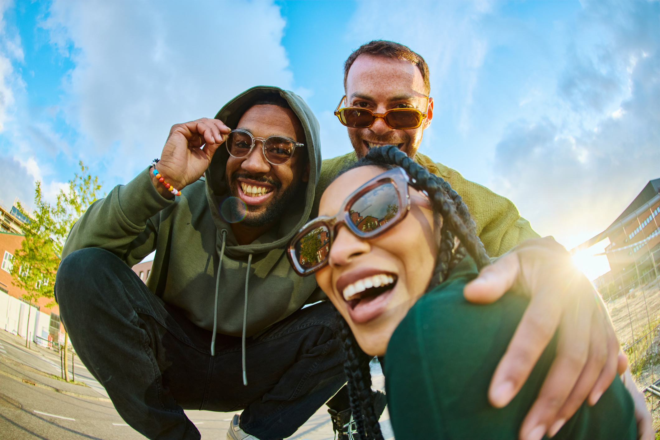Three cheerful young adult friends are laughing together outdoors, enjoying their time and wearing sunglasses