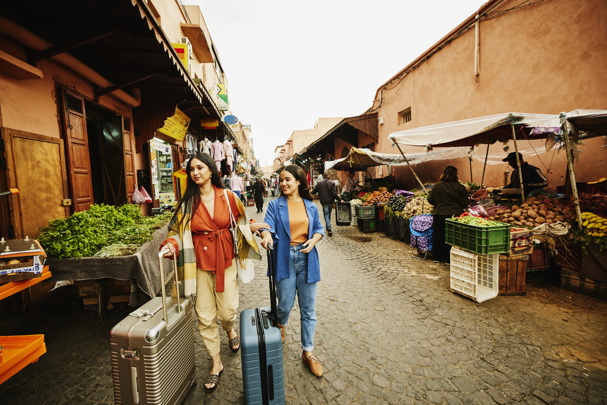 Wide shot of female friends walking with luggage through the souks of Marrakech while on vacation