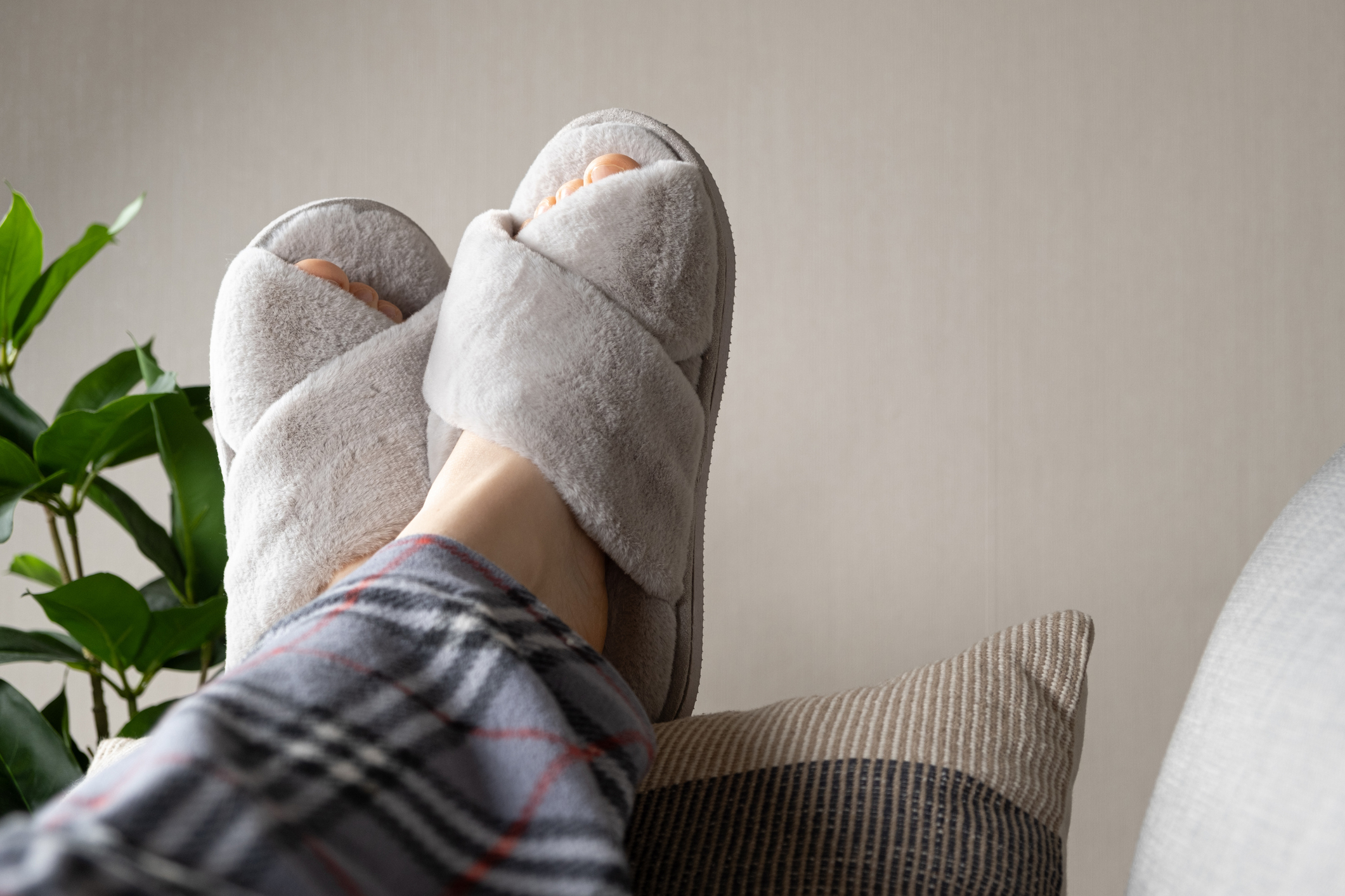Stylish modern grey house slippers on women's feet lying on sofa.