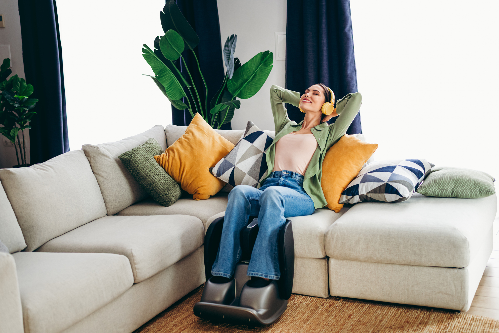 A woman sits on her couch, using a foot massager.