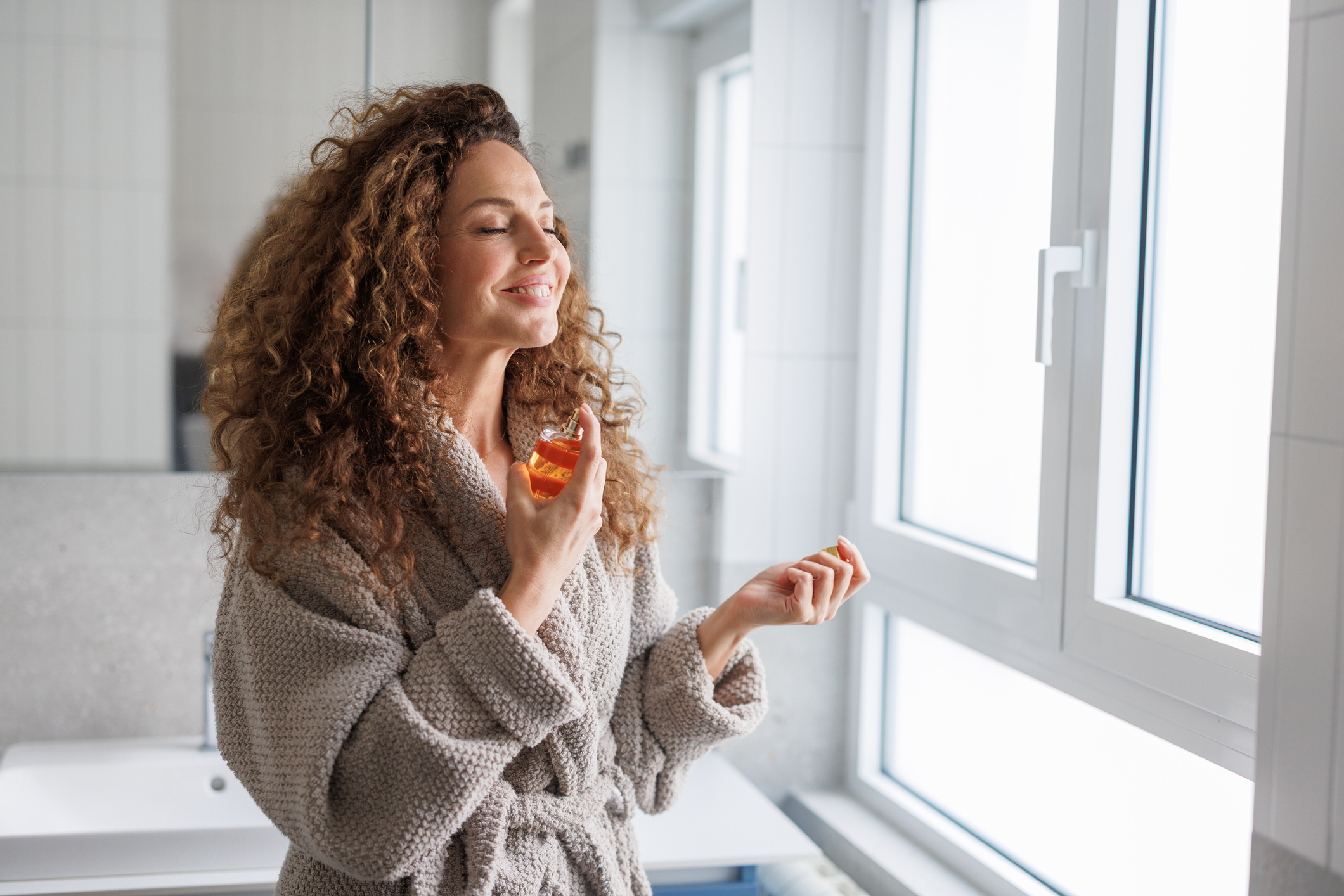 A woman spraying on perfume in a bathroom.