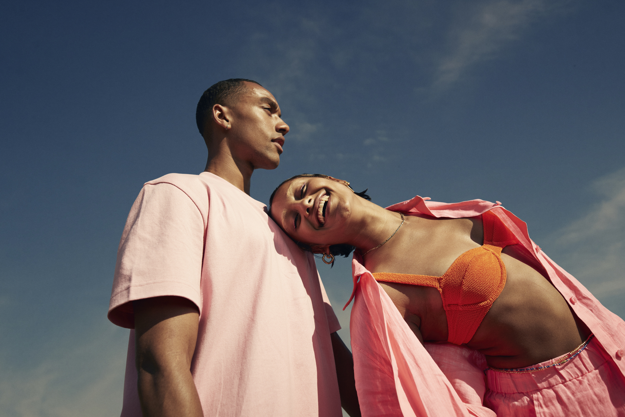 Carefree young woman leaning on male friend while standing against sky