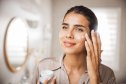 Young woman applying moisturizing cream on face in front of mirror in bathroom