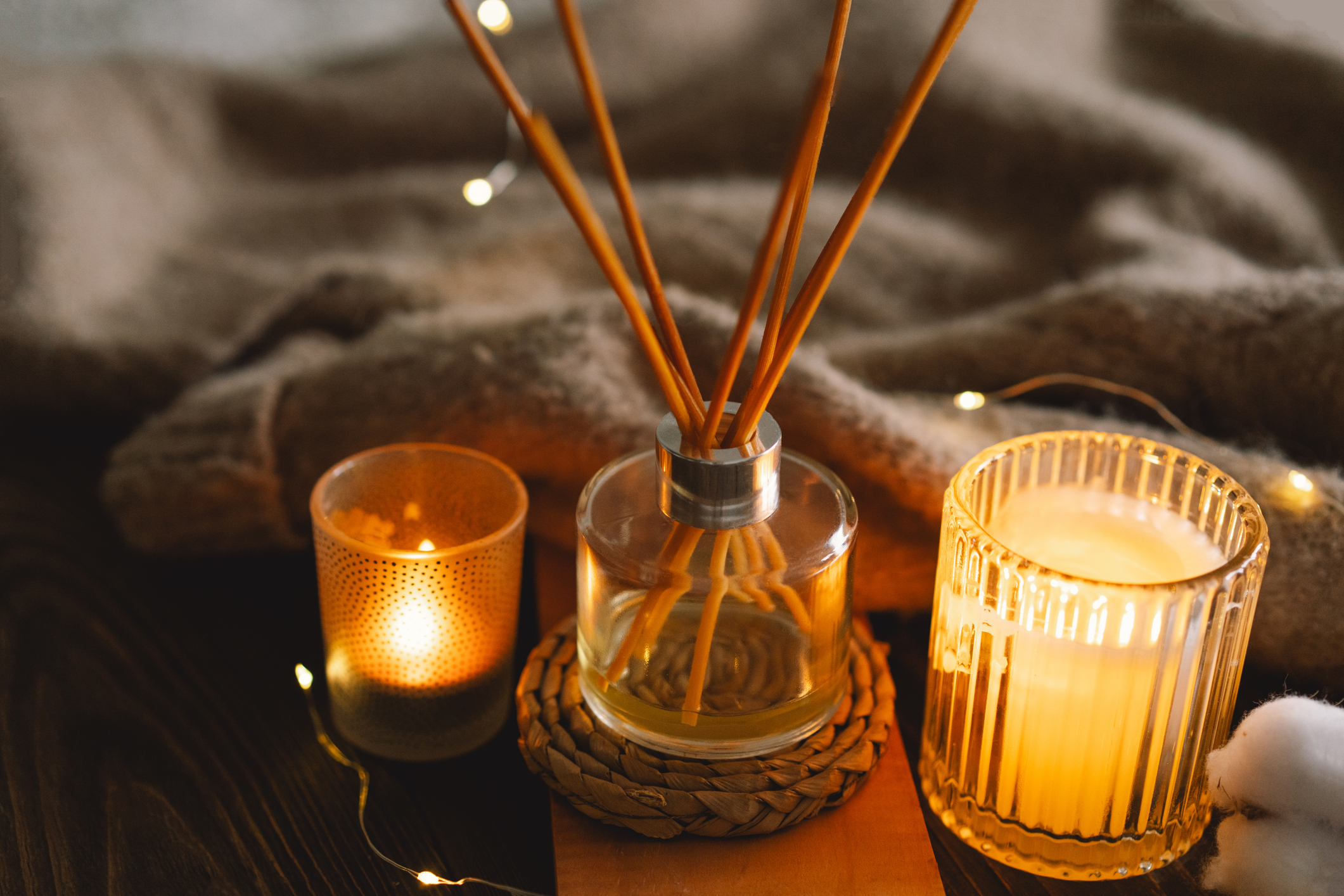 Home perfume or stick perfume in glass bottle with wood sticks. Burn candles on wood tray in bedroom. Aromatherapy Concept. Winter warm Christmas season.