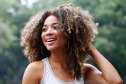 Young Latina woman with afro hair, laughing in park.