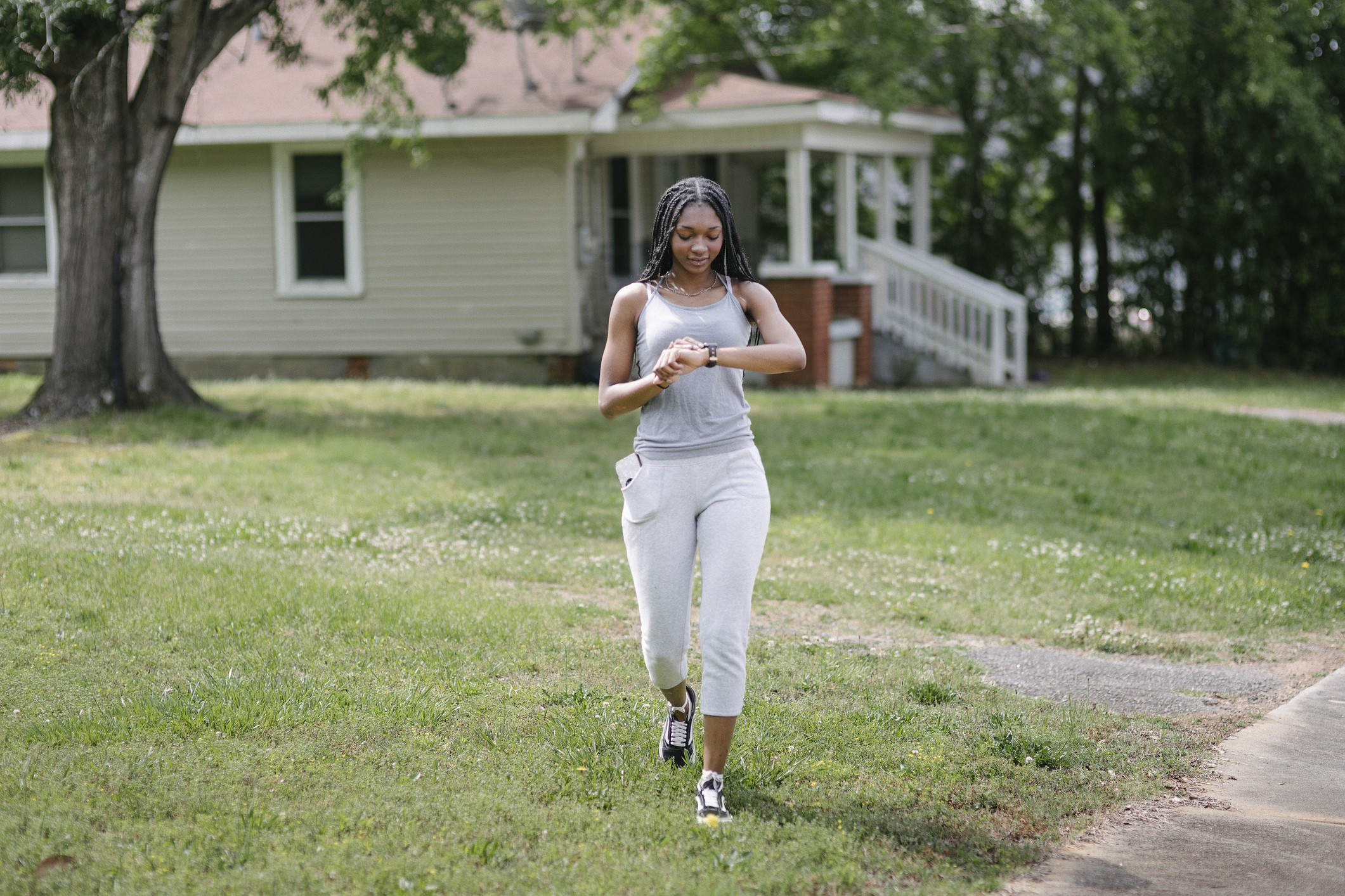 A woman with long hair checking her watch while out jogging in her neighborhood.