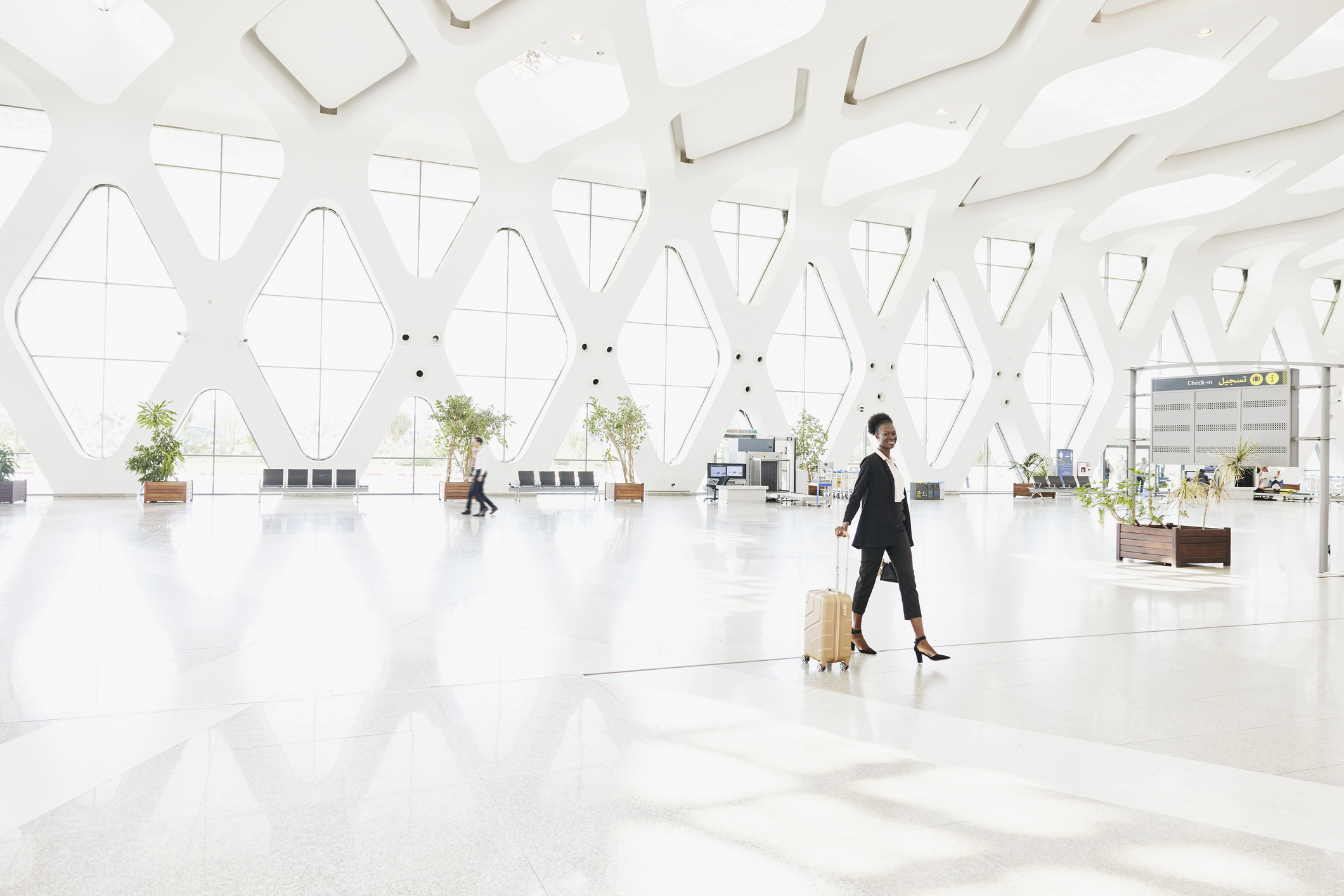 Extreme wide shot of smiling businesswoman walking through airport terminal with luggage
