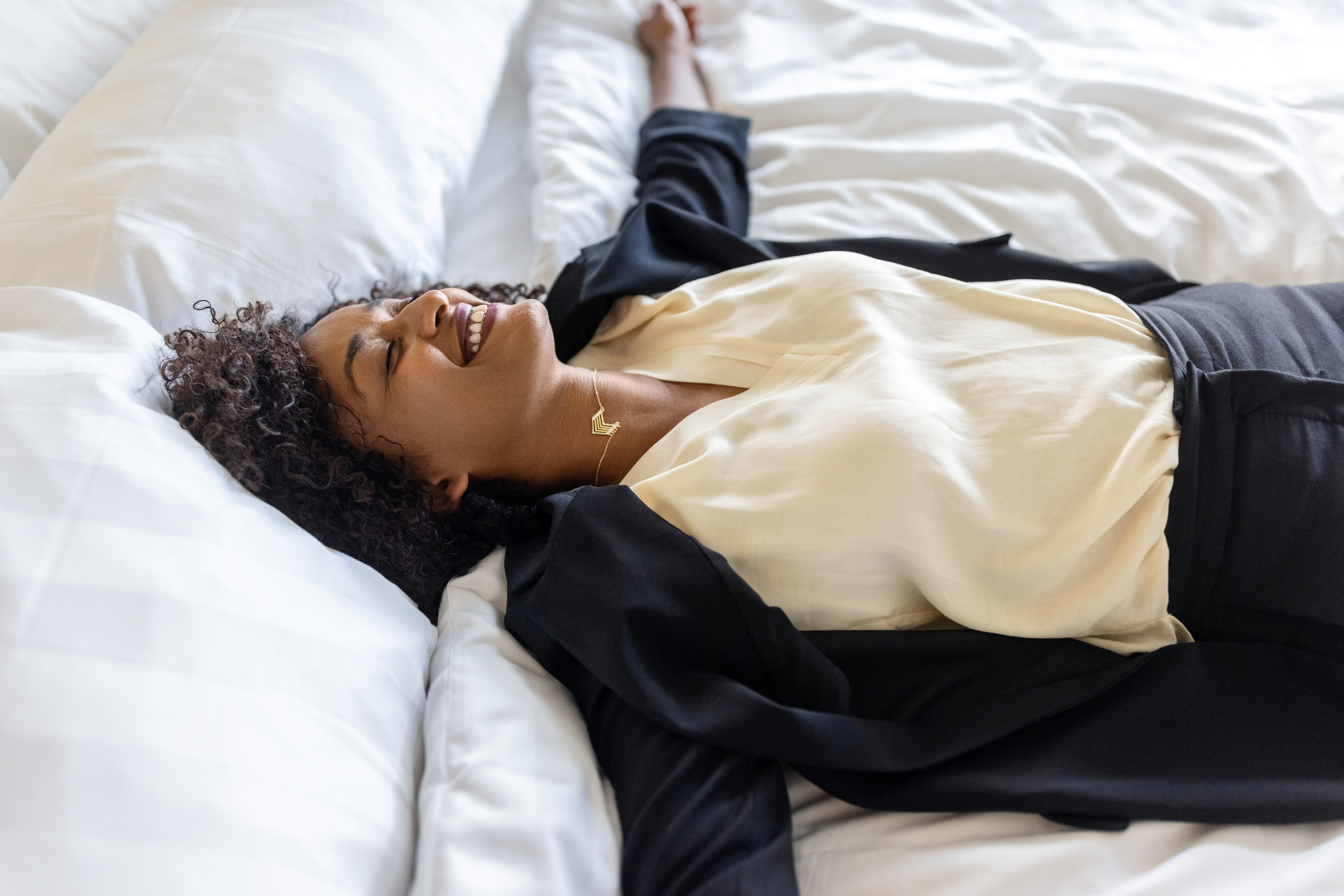 Tired mid adult businesswoman lying on hotel bed after her trip. Tired woman in formal clothes resting on hotel bed with her arms outstretched and smiling.