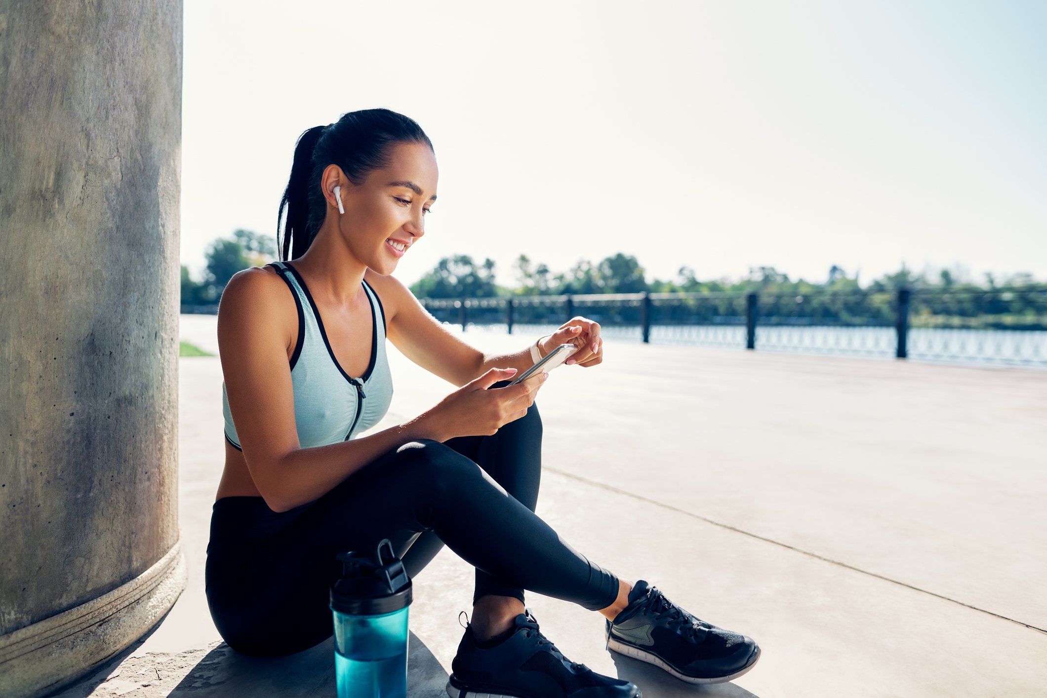 Happy fit woman holding smartphone and counts calories in sport app after running. Sport, break concept
