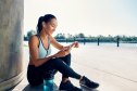 Happy fit woman holding smartphone and counts calories in sport app after running. Sport, break concept