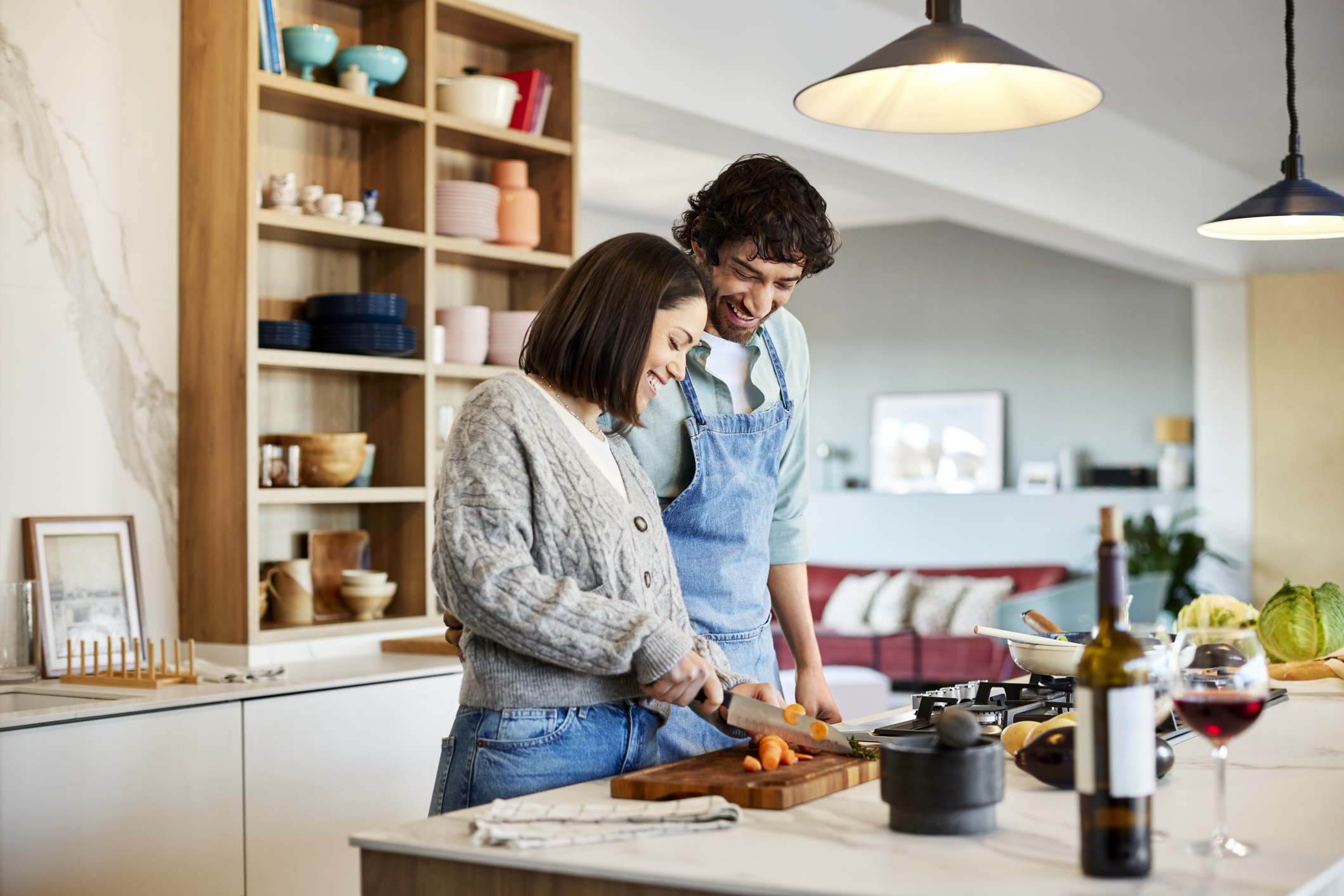 Smiling man looking at woman chopping carrot. Happy couple is cooking food together at home with the Emeril Lagasse air fryer.