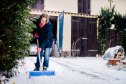 Woman shoveling snow in the yard in front of car.