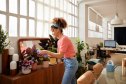 Side view of young woman cleaning leaves of plotted plants at home. Woman with curly hair gardening at home. She is wearing casuals.