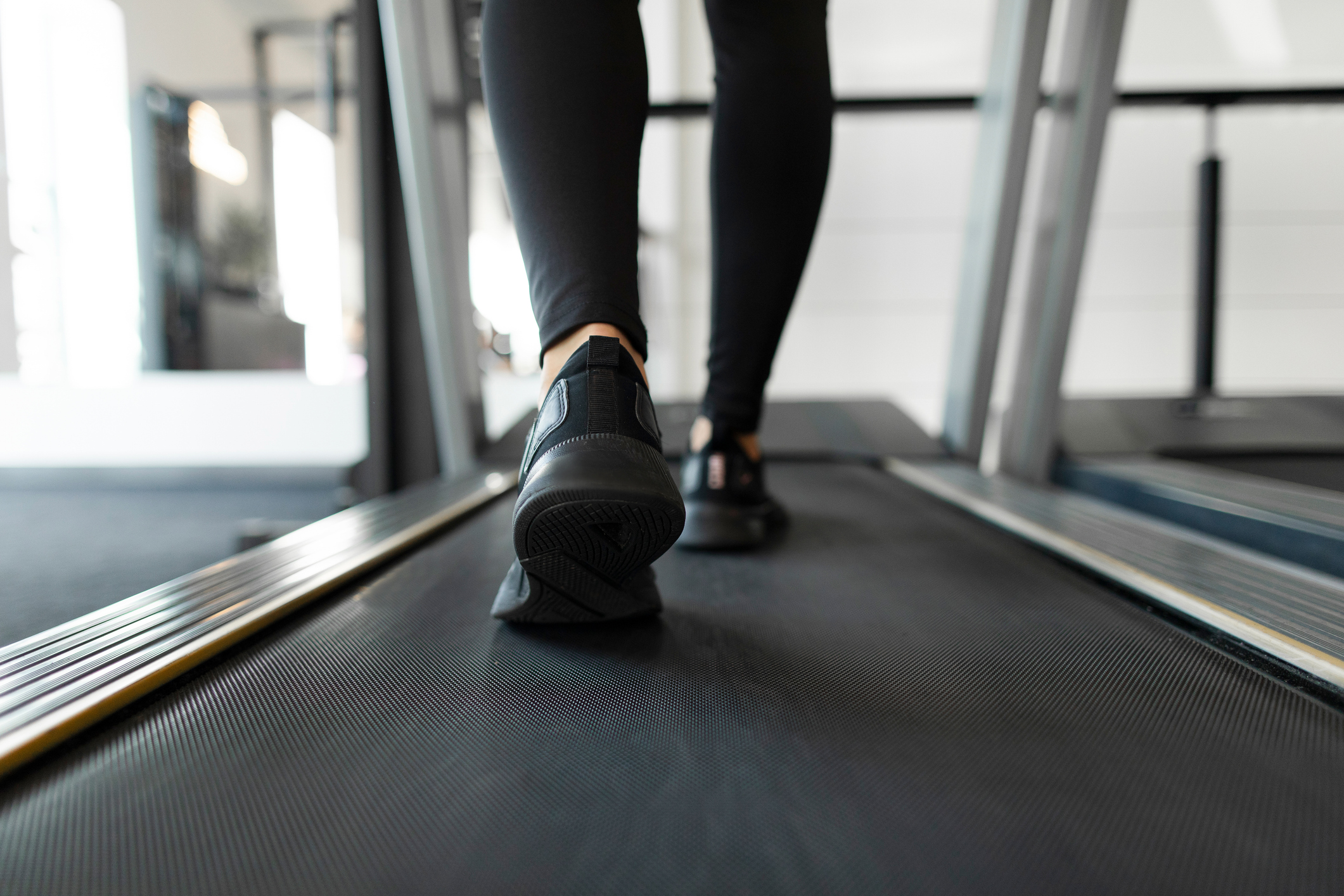 Slender lady in sportswear doing cardio workout on treadmill in the gym, shot with focus on feet, back view. Running activity