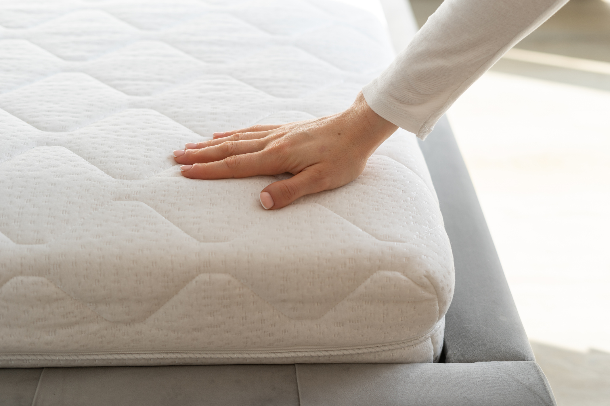 Woman hand testing white and new orthopedic mattress on firmness, cropped shot. Female pressing hypoallergenic foam topper to check its softness