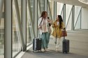 Full length of smiling businesswomen talking while walking with luggage on elevated walkway