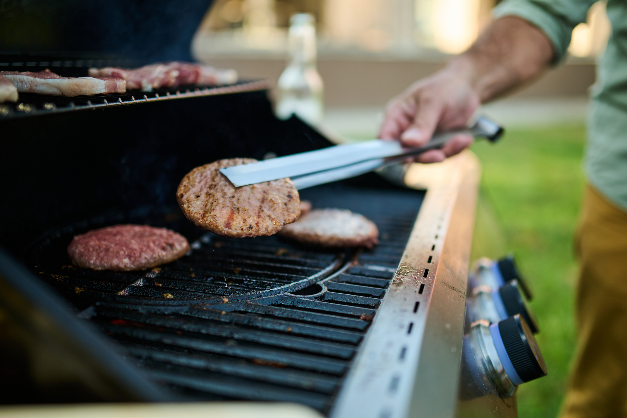 Grilling burgers and sausages outdoors in the backyard on a sunny day, surrounded by friends and family