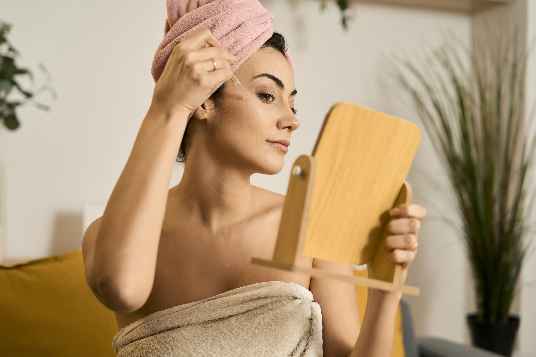 Young adult woman applying facial serum to her face after a shower for daily skincare