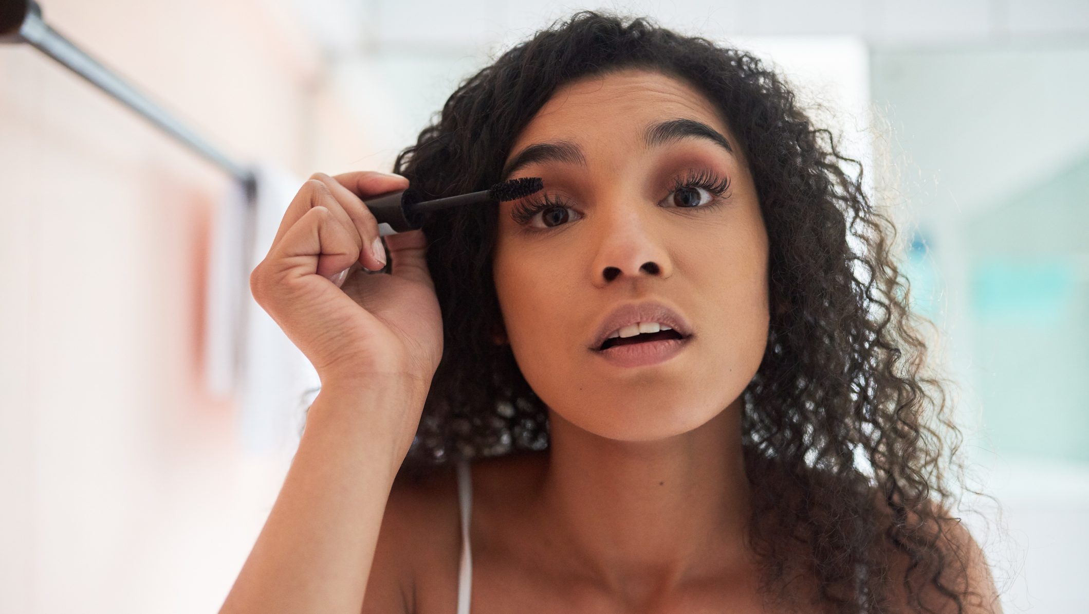 Portrait of an attractive young woman applying mascara in the bathroom