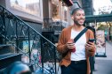 Cheerful mid adult man walking with smart phone in city. He has just received a text message with good news.