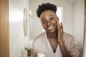 Young woman in bathroom applying moisturizing cream on her skin after having a bath.