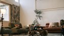 cozy living room featuring mid-century style armchairs, a leather sofa with patterned pillows, a floor lamp, and a stone accent wall, creating a warm and inviting bungalow interior.