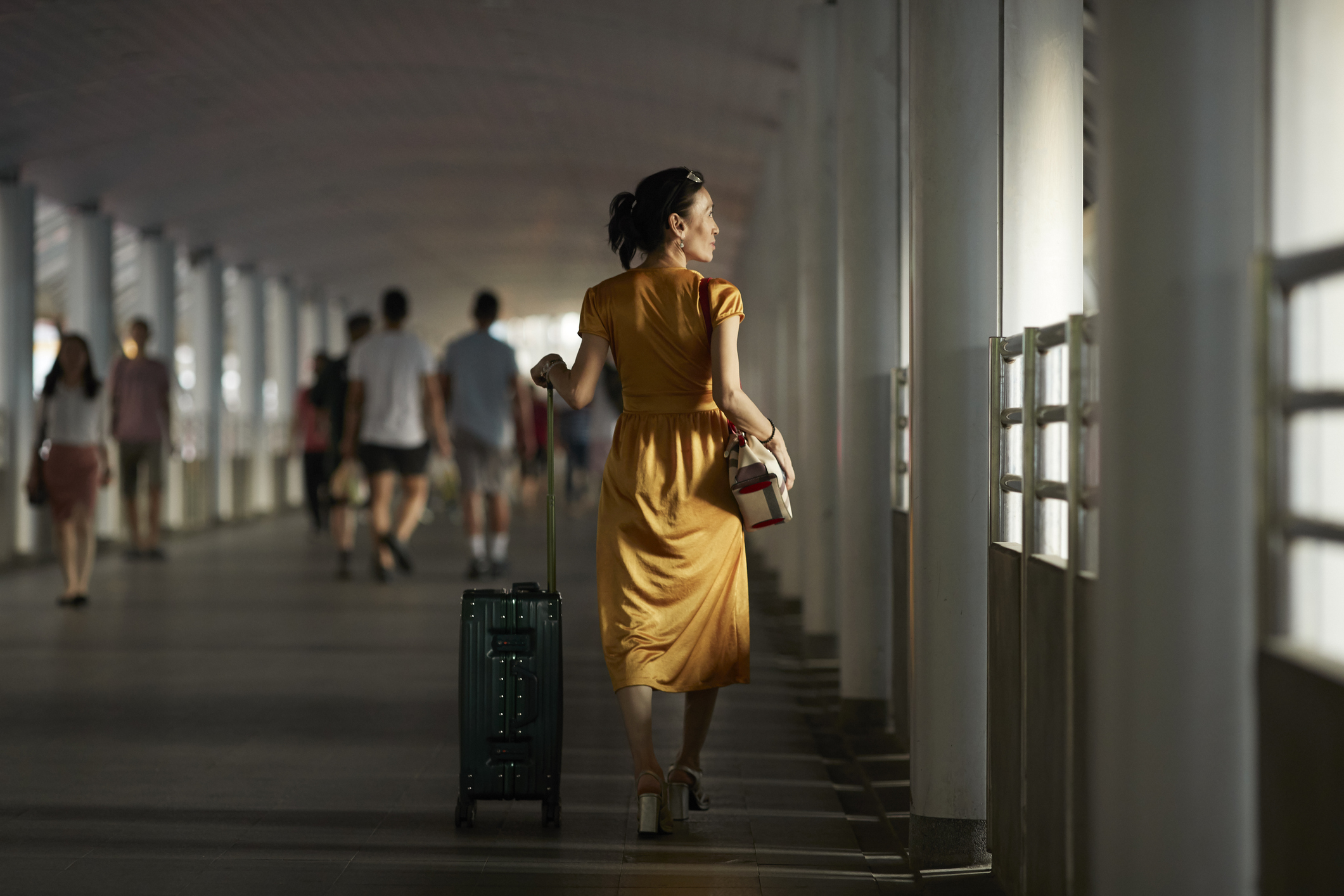 Full length rear view of woman with luggage walking on bridge at railroad station