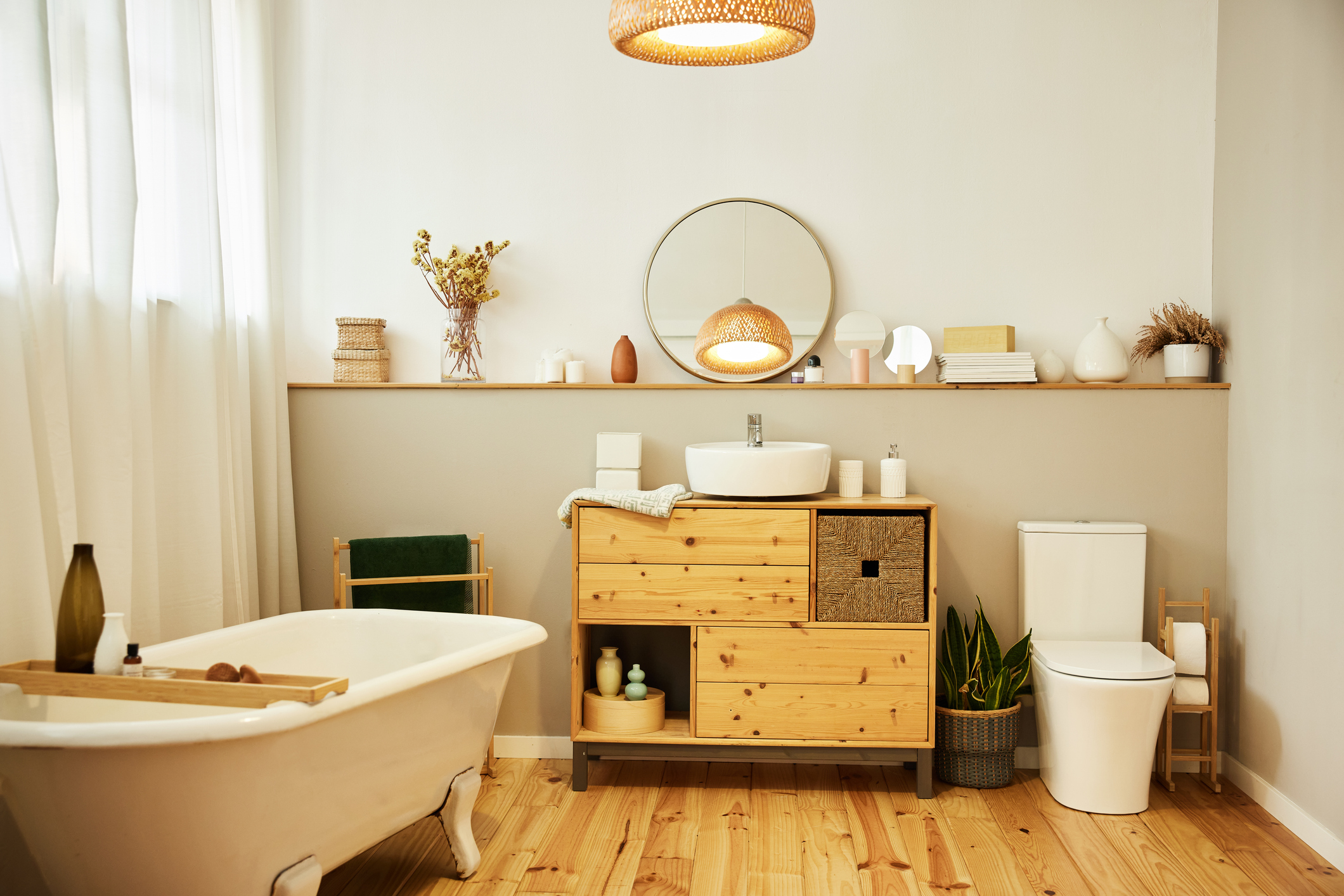 Sink with toiletries kept on cabinet by bathtub. Reflection of lighting equipment is on mirror. Interior of modern bathroom.