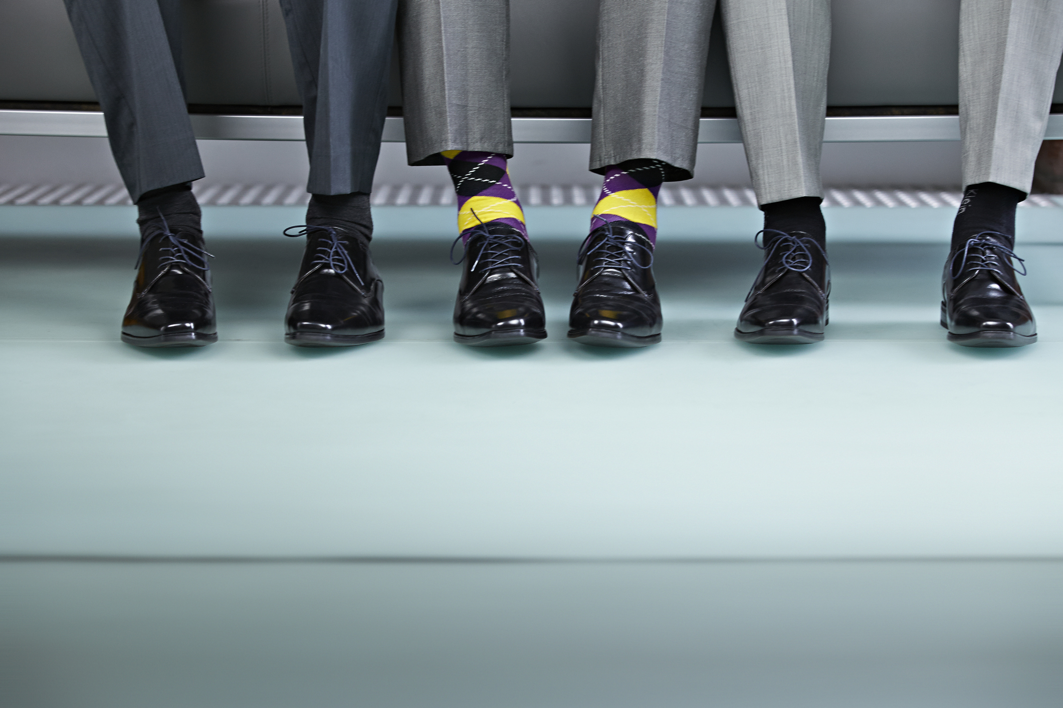 Three men sitting on bench, view of shoes