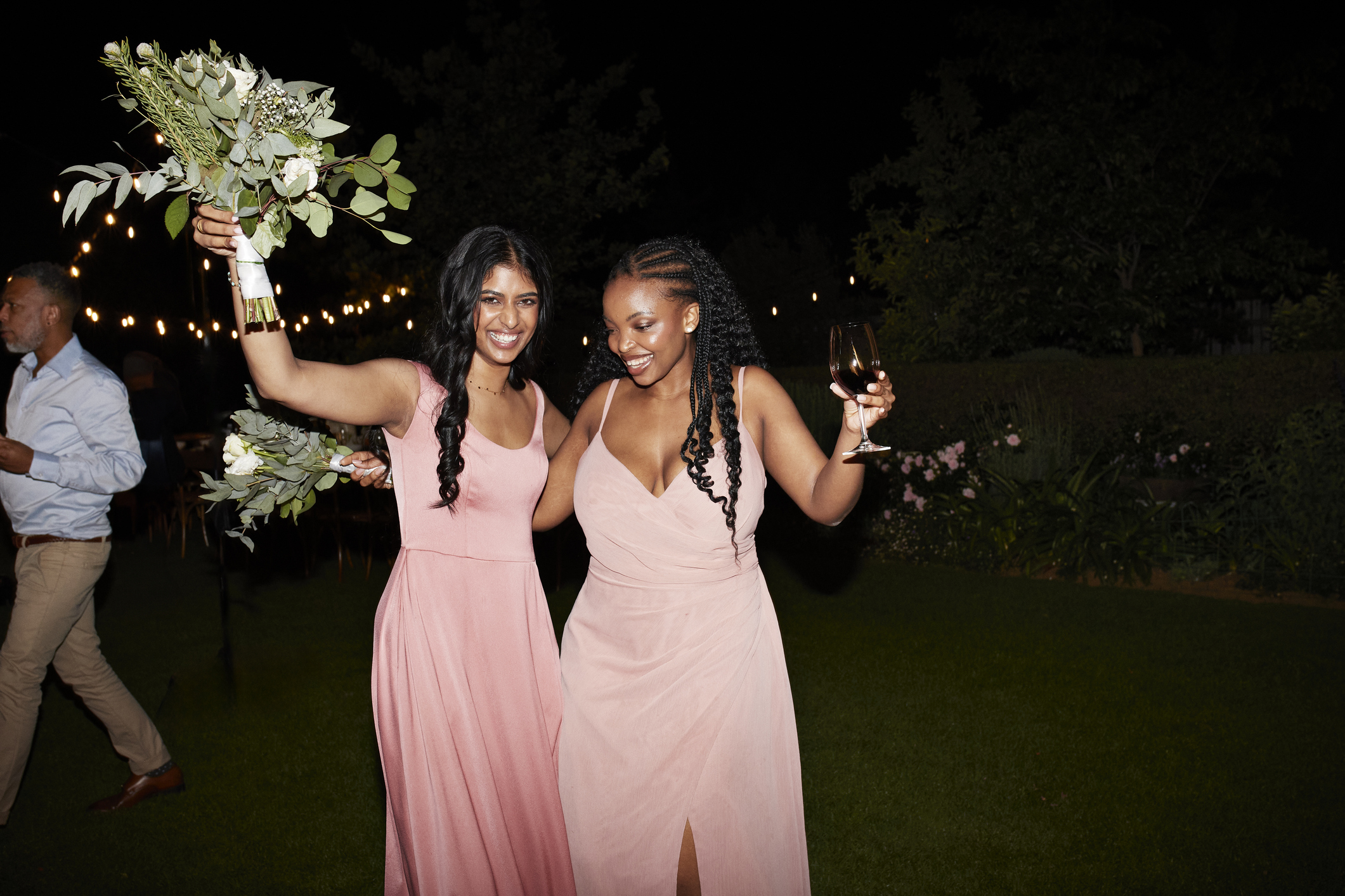 Cheerful young multiracial bridesmaids holding flower bouquets while dancing at wedding reception during night