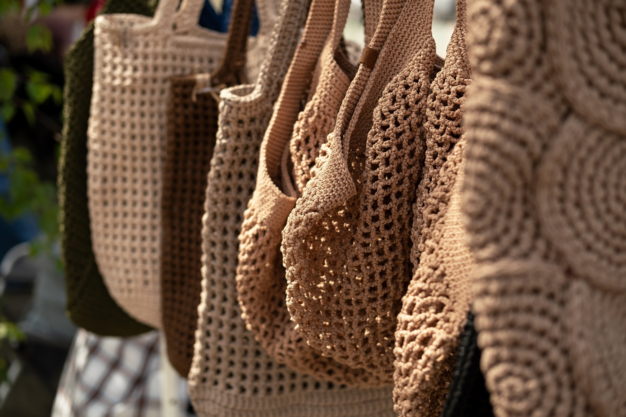 A beige and natural colors display of crochet bags in diverse patterns hangs neatly at a market stall. Lively and inviting shopping scene at outdoor market